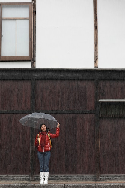 Mujer con paraguas transparente en lluvioso con pared de madera. Concepto de temporada de lluvias.