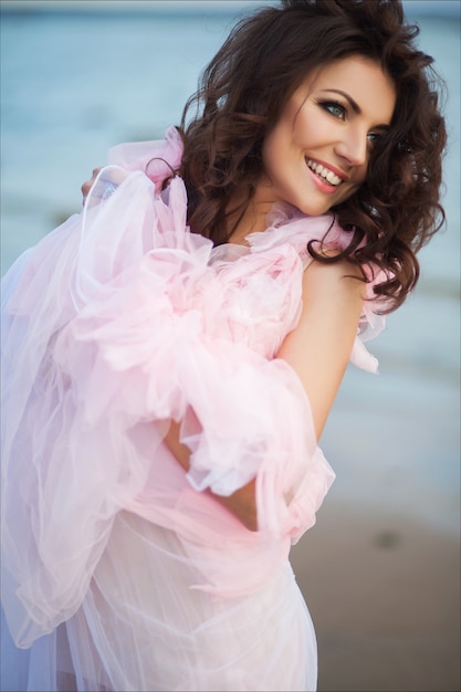 Mujer de paraíso de vacaciones pacíficas caminando en la playa del océano al atardecer. Niña emocionada sonriente en vestido rosa romántico