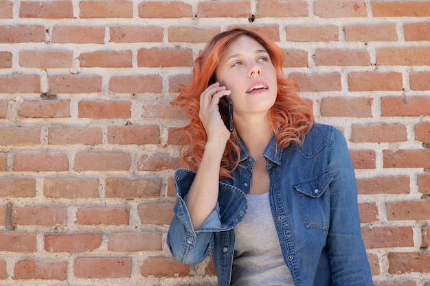 mujer en la pared de ladrillo hablando por teléfono celular