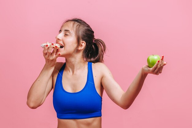 mujer en una pared rosa sosteniendo un pastel y una manzana