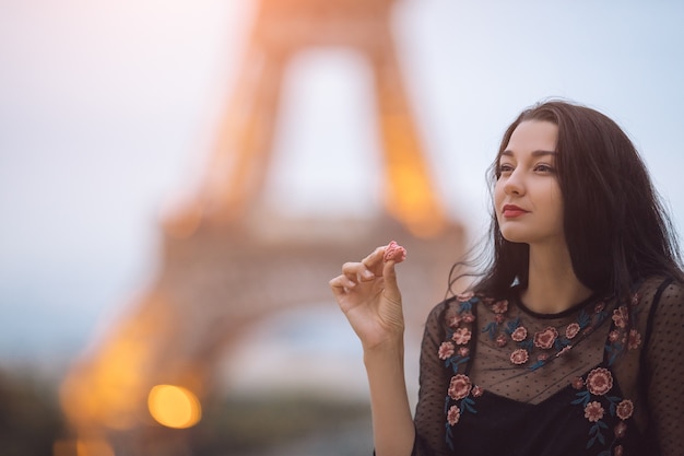 Foto mujer de parís sonriendo comiendo el macarrón de pastelería francesa en parís contra la torre eiffel.