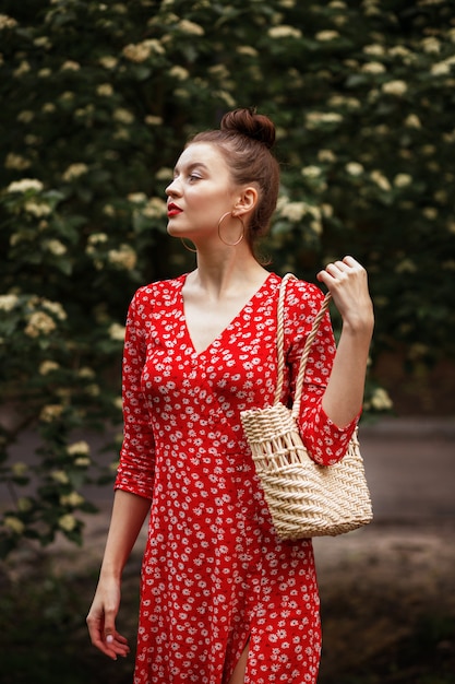 Mujer en el parque con una bolsa de mimbre de verano. vestido rojo