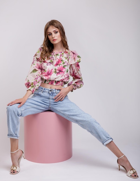 Mujer en la parte superior de la blusa con estampado de flores en rojo blue jeans modelo sentado en el cilindro de cubo rosa