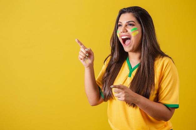 Mujer partidaria del campeonato de fútbol de la copa mundial de Brasil 2022 sorprendida increíble señalando con los dedos hacia la izquierda