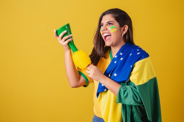 Mujer partidaria del campeonato de fútbol de la copa mundial de Brasil 2022 usando la bandera de Brasil como tapadera tocando la bocina y festejando en el partido de fútbol Horn