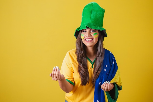 Mujer partidaria de la copa mundial de brasil 2022 llamando con sus manos ven bienvenida con una bandera y un sombrero de brasil