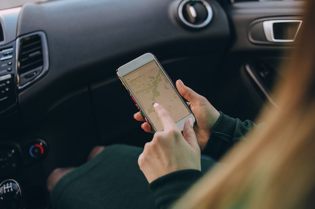 Mujer pasajera en un automóvil con un mapa en un teléfono inteligente prepara una ruta