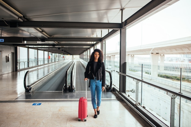 Mujer en la pasarela móvil en el aeropuerto con una maleta rosa.