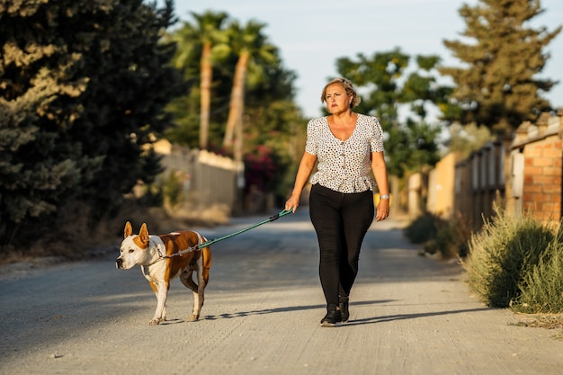 Mujer paseando a un perro en una calle sin pavimentar