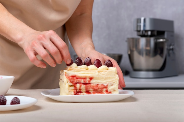 Mujer pastelera decora pastel con bayas. Pastel de crema de vainilla con relleno de frutos rojos.