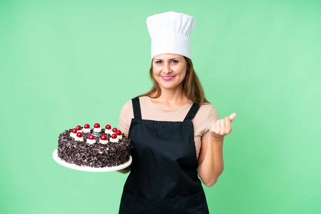 Mujer pastelera de mediana edad sosteniendo un gran pastel sobre un fondo aislado haciendo gestos de dinero