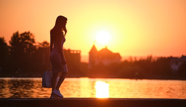 Mujer peatonal solitaria caminando sola al lado del lago en una tarde cálida Concepto de soledad y relajación