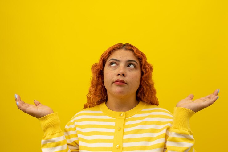 Foto mujer con pecas con expresión reflexiva con las manos en un fondo amarillo