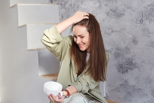 Mujer con pecas naturales disfrutando del sol de la mañana mientras está sentada en las escaleras de su casa.