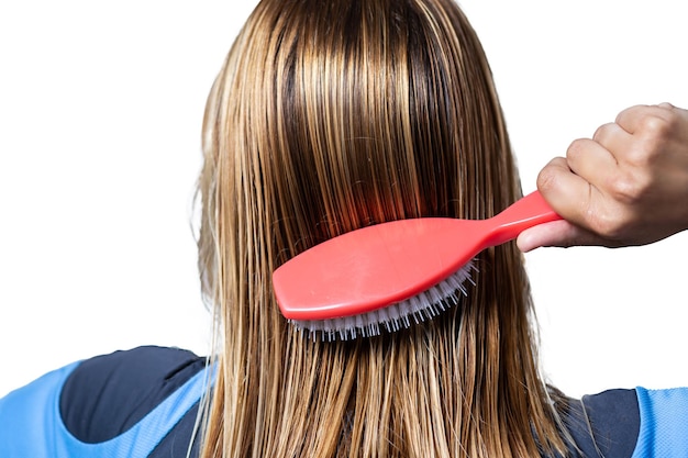 Mujer peinándose el cabello mojado con un peine de masaje sobre un fondo blanco.