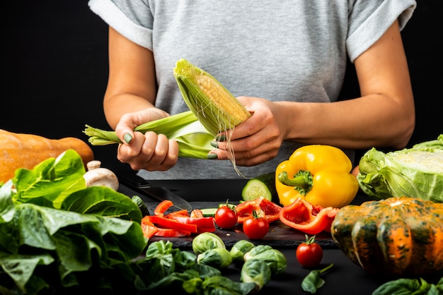 Mujer pelando una mazorca de maíz, cocinar diferentes verduras. Concepto de comida vegetariana saludable.