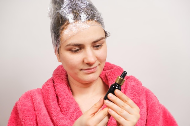 Una mujer con una película en la cabeza sostiene una botella de aceite natural para el cabello