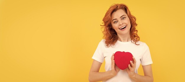 Mujer pelirroja alegre sostener corazón de amor sobre fondo amarillo cariño Mujer cara aislada retrato banner con espacio de copia