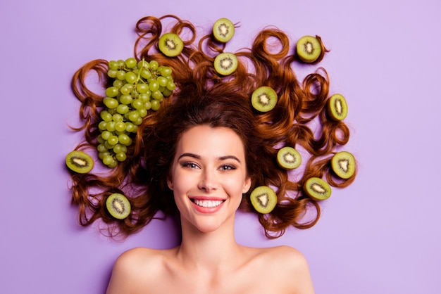Mujer pelirroja artística posando con kiwi y uva en el pelo