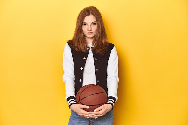 Mujer pelirroja atlética con fondo de estudio amarillo baloncesto