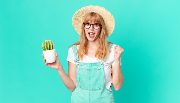 Mujer pelirroja bastante sorprendida, riendo y celebrando el éxito y sosteniendo un cactus en maceta. concepto de granjero