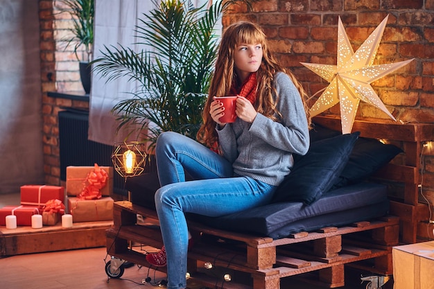 Mujer pelirroja bebe un café caliente en una sala de estar con interior de loft.