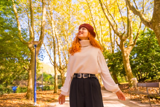 Mujer pelirroja con boina en un bosque de la ciudad del parque al atardecer disfrutando del otoño