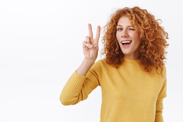 Mujer pelirroja con cabello rizado satisfecha con su nuevo look mostrando la paz y el signo de la victoria