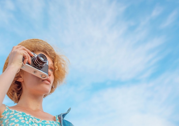 Mujer pelirroja con cámara vintage y tomar fotografías sobre fondo de cielo azul
