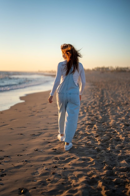 Mujer pelirroja caminando por la playa mientras mira el mar