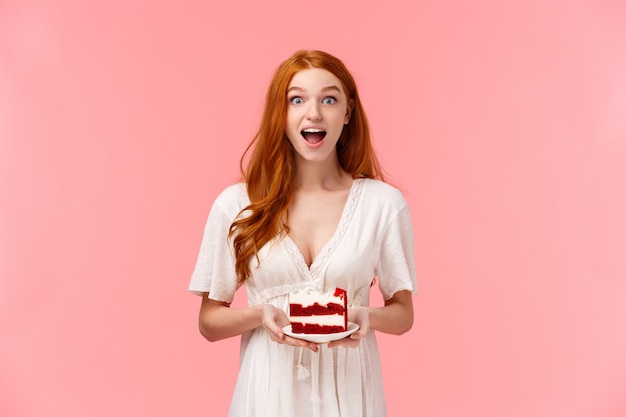 Mujer pelirroja carismática sorprendida y divertida que cotillea durante la fiesta, sosteniendo el plato con pastel