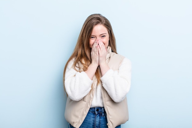 Mujer pelirroja caucásica que se ve feliz, alegre, afortunada y sorprendida cubriendo la boca con ambas manos