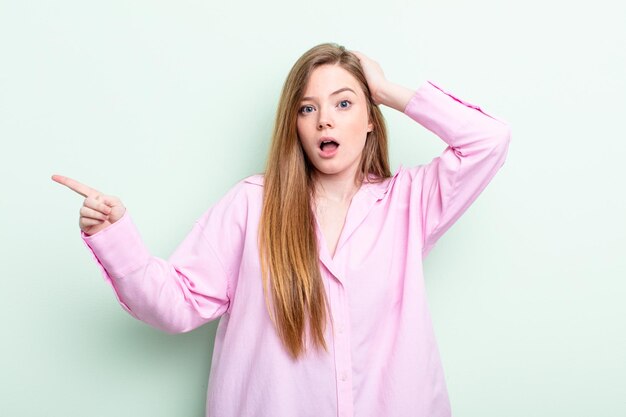 Mujer pelirroja caucásica riendo, luciendo feliz, positiva y sorprendida, dándose cuenta de una gran idea que apunta al espacio de copia lateral