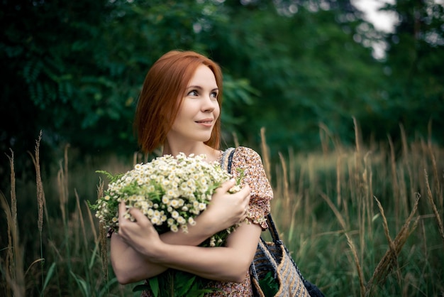 Mujer pelirroja de cuarenta años con un gran ramo de flores silvestres en verano en la naturaleza