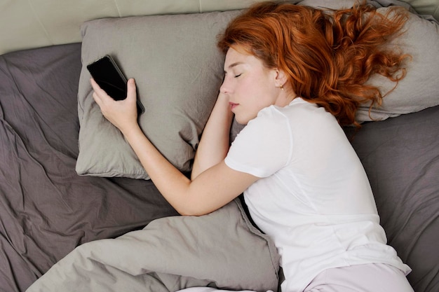 Foto mujer pelirroja durmiendo con el teléfono celular en la mano