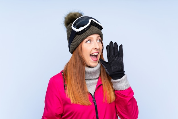 Mujer pelirroja esquiador con gafas de snowboard sobre pared azul aislado gritando con la boca abierta