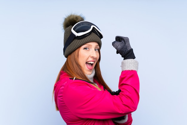 Mujer pelirroja esquiador con gafas de snowboard sobre pared azul aislado haciendo un gesto fuerte