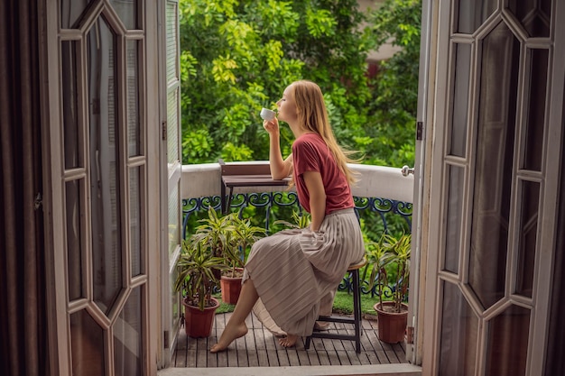 Una mujer pelirroja está de pie en un balcón de estilo heritage disfrutando de su café de la mañana una mujer en un