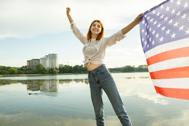 Mujer pelirroja feliz con la bandera nacional de los Estados Unidos en la mano Chica positiva celebrando el día de la independencia de los Estados Unidos