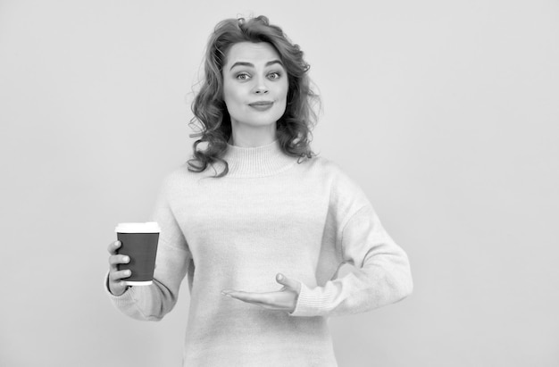 Mujer pelirroja feliz que presenta el producto del café para llevar en una taza de café