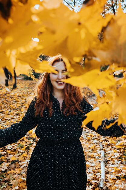 Mujer pelirroja feliz sosteniendo hojas de otoño de arce amarillo en el parque de otoño Retrato de mujer joven pelirroja alegre con hojas de otoño