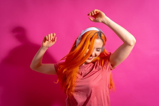 Foto mujer pelirroja en fotografía de estudio bailando sonriendo sobre un fondo rosa