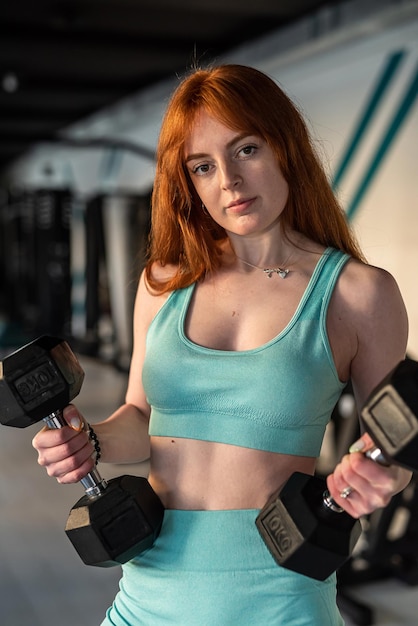Mujer pelirroja fuerte haciendo ejercicio con pesas en el gimnasio Entrenamiento físico con pesas rusas en interiores