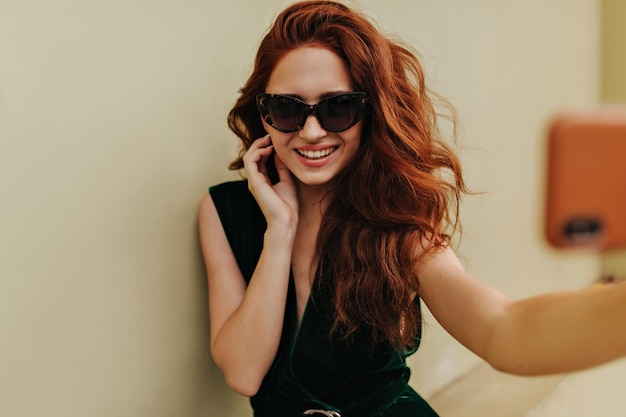 Mujer pelirroja con gafas de sol sonriendo y tomando selfie