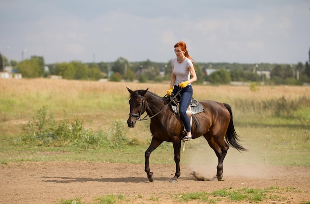 Una mujer pelirroja con guantes amarillos montando un caballo en la naturaleza