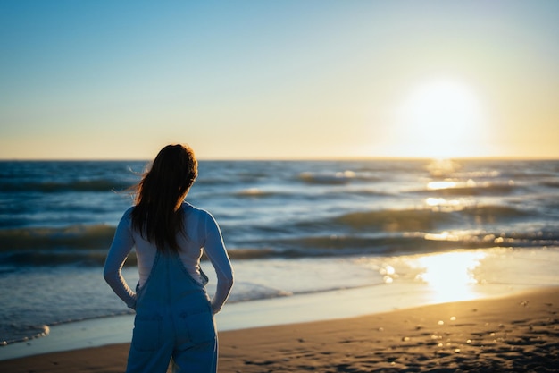 Mujer pelirroja irreconocible en la playa viendo la puesta de sol