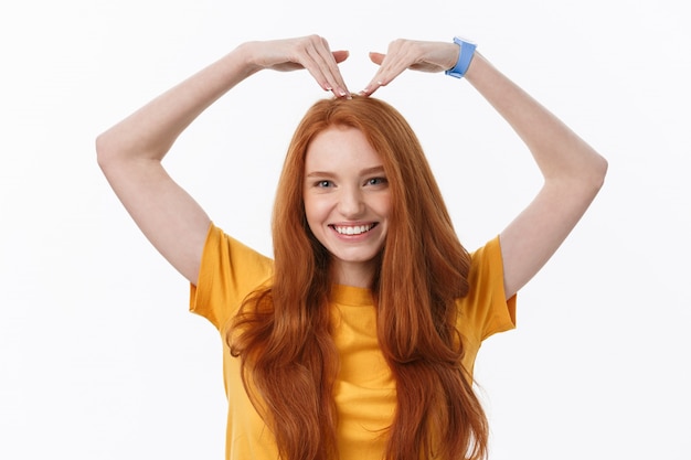 Mujer pelirroja joven bastante romántica haciendo un gesto de corazón con una sonrisa tierna y feliz