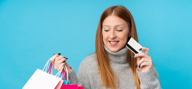 Mujer pelirroja joven con bolsas de compras y una tarjeta de crédito