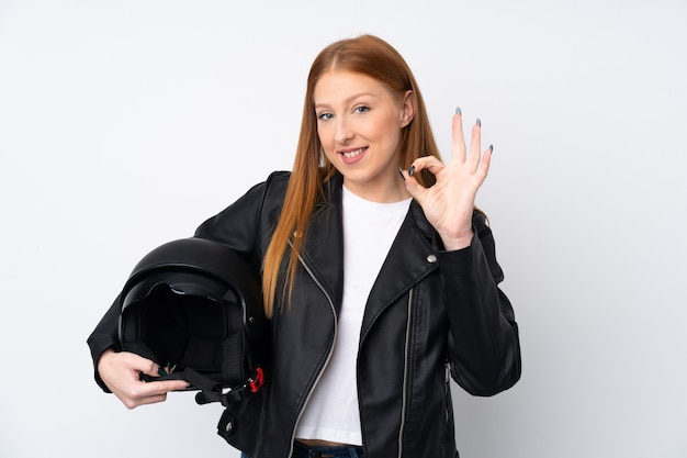 Mujer pelirroja joven con un casco de moto sobre pared blanca aislada mostrando signo bien con los dedos