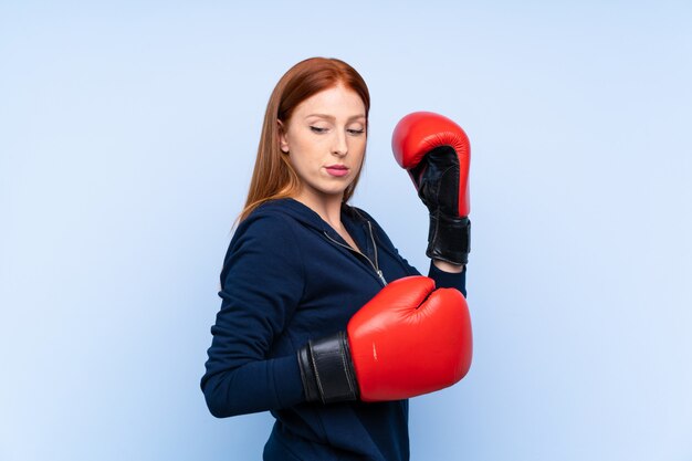 Foto mujer pelirroja joven deporte sobre pared azul aislado con guantes de boxeo